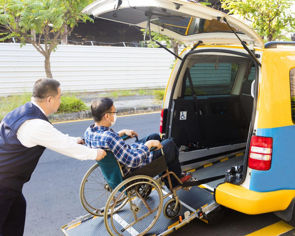 driver helping man on wheelchair getting into taxi